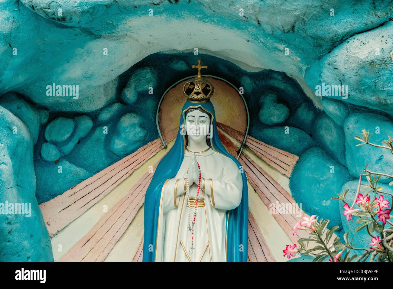 Une statue sereine de la Vierge Marie, couronnée Reine du ciel et tenant un chapelet, est enchâssée dans une grotte bleue brillamment peinte Banque D'Images