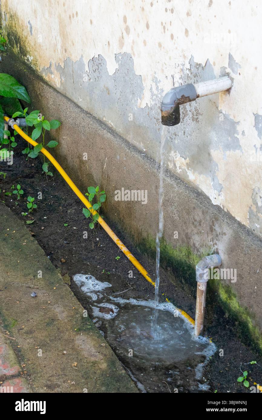 Le tuyau jaune coule de l'eau sur le sol. L'eau sort d'un tuyau fixé à un mur Banque D'Images