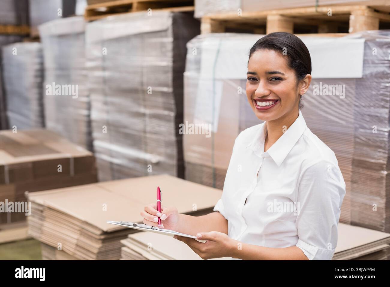 Femme hispanique vérifiant l'inventaire avec presse-papiers et stylo rouge dans la zone de stockage de l'entrepôt, espace de copie Banque D'Images