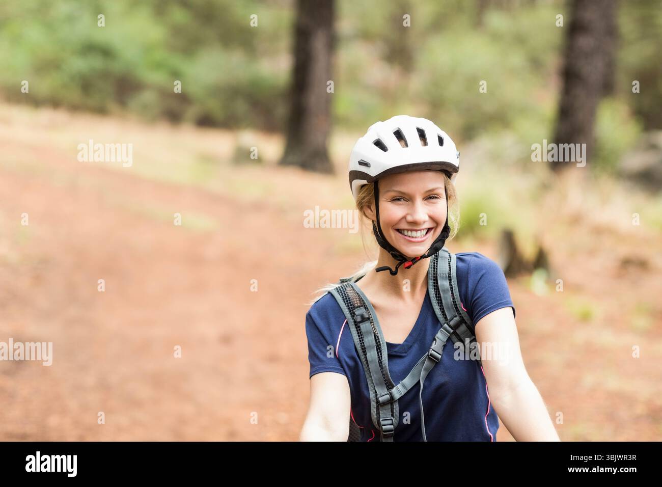 Femme à vélo portant un casque blanc et un pack d'hydratation gris sur le sentier rouge de forêt de terre Banque D'Images