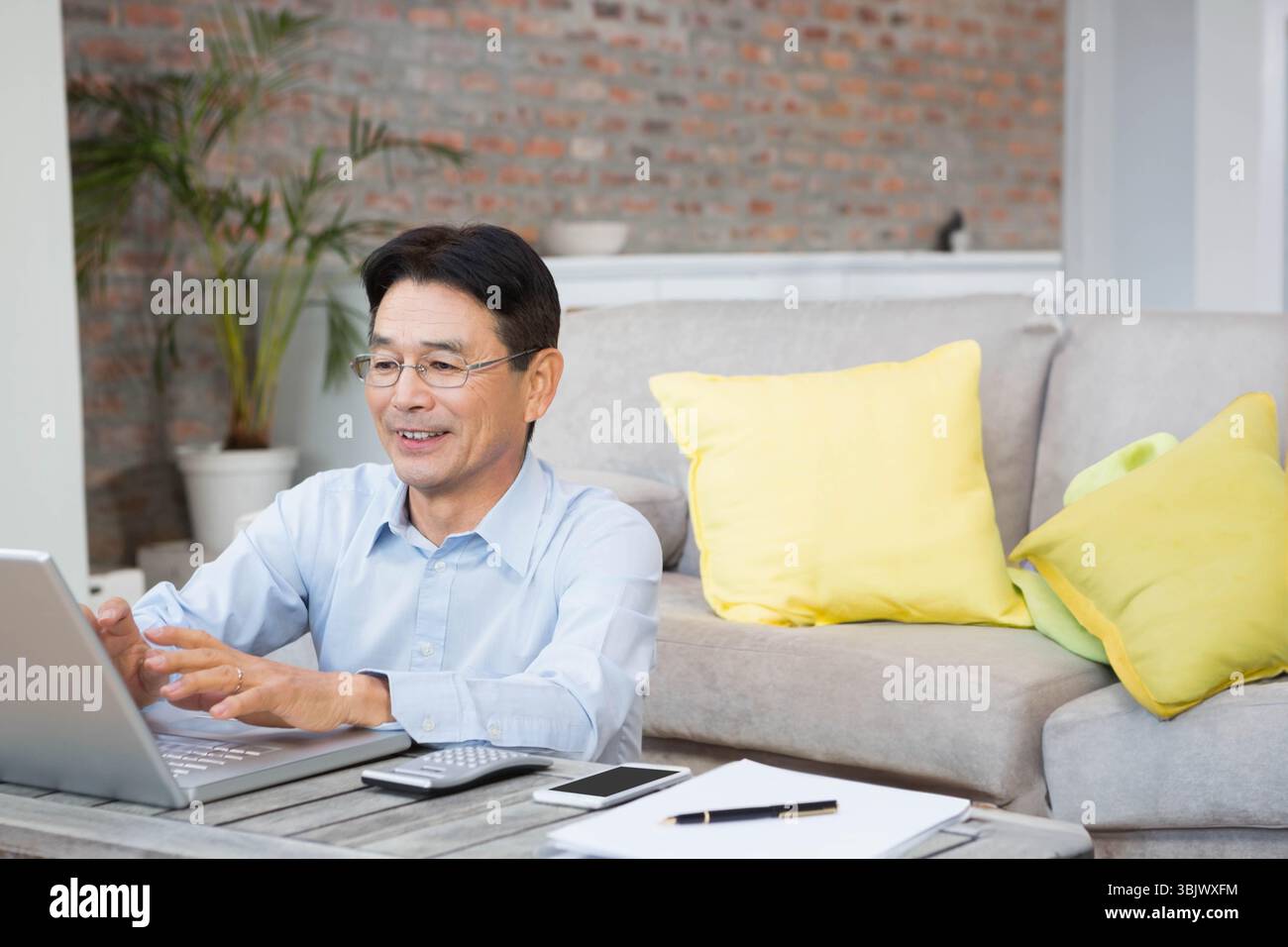 Homme japonais senior tapant sur ordinateur portable à la table basse du salon avec des papiers de calculatrice de smartphone Banque D'Images