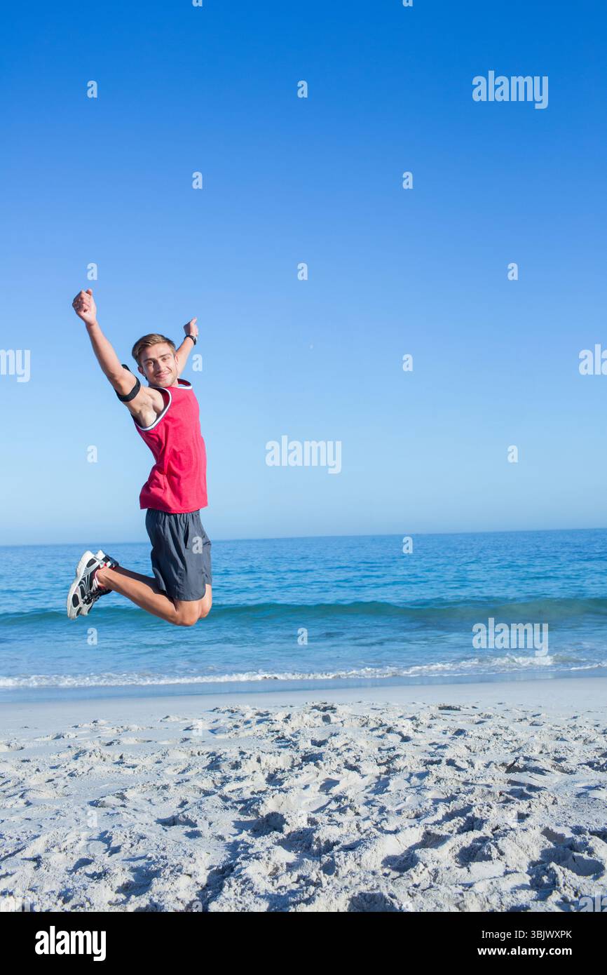 Homme sautant sur le rivage de sable portant des baskets blanches à brassard noir rouge, espace copie Banque D'Images Homme sautant sur le rivage de sable portant des baskets blanches à brassard noir rouge, espace copie Banque D'Images