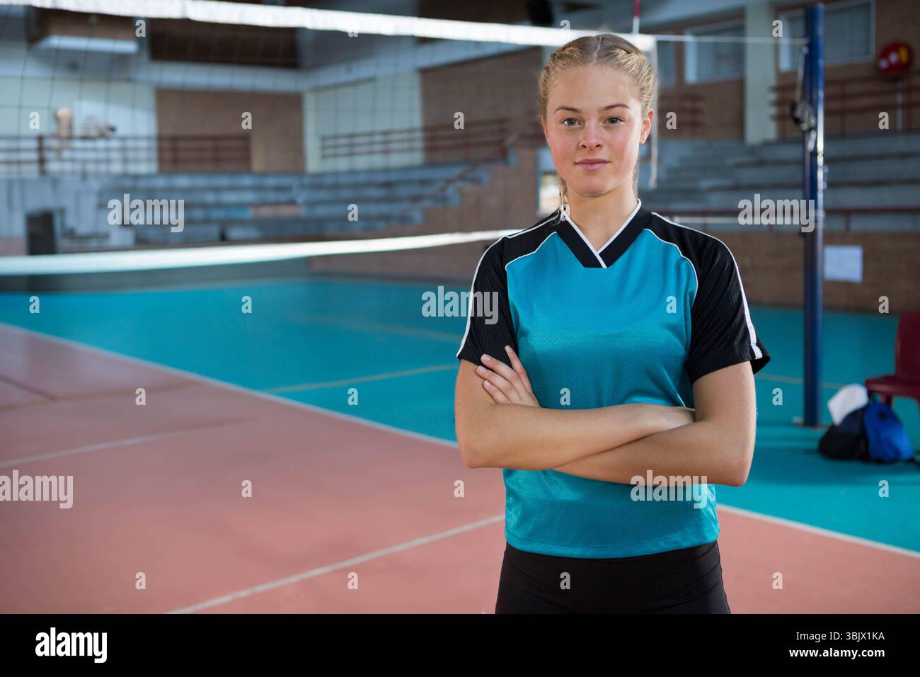 Joueuse de volley-ball adolescente debout près du poteau de soutien du filet dans la salle de gym avec sac de sport sur la chaise Banque D'Images