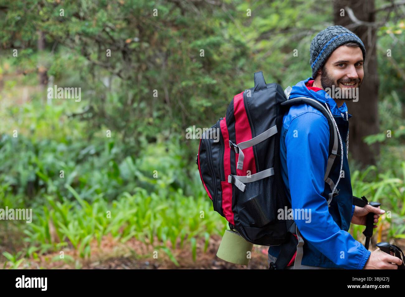 Homme à la fin de la vingtaine sentier forestier marchant avec sac à dos rouge et bâtons de randonnée, espace de copie Banque D'Images