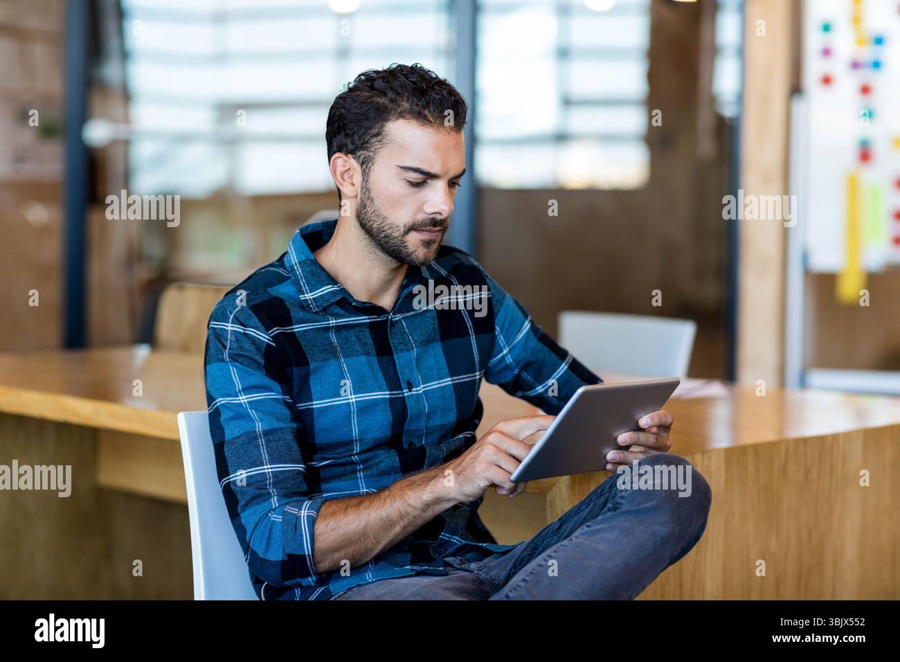 Employé de bureau assis sur la chaise en utilisant la tablette à la table près de la cloison en verre avec des notes adhésives Banque D'Images