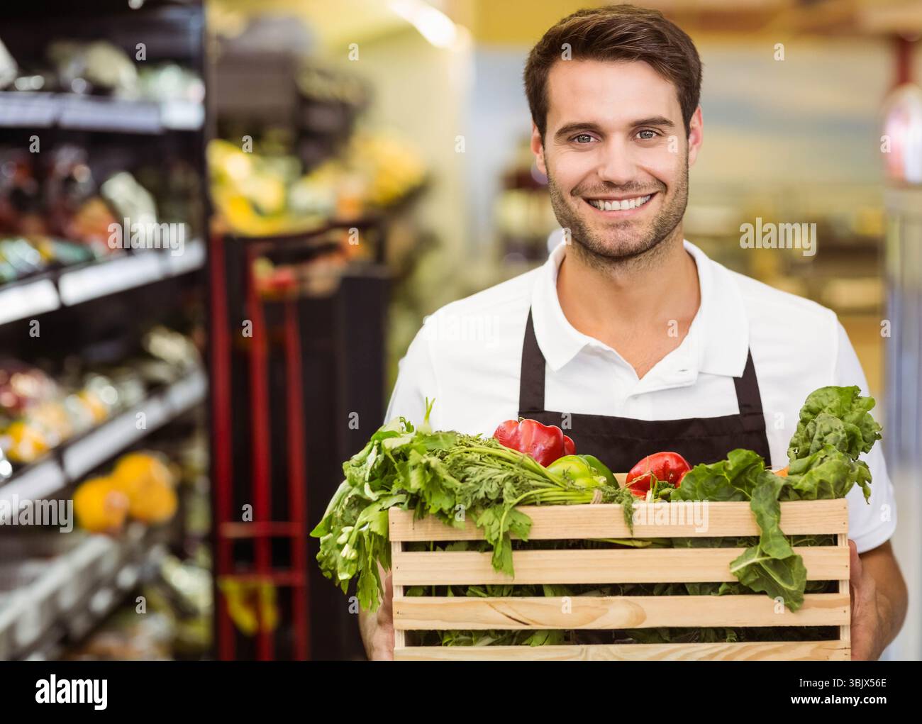 Homme tenant une caisse en bois avec des poivrons rouges et verts, des verts feuillus et des herbes dans la section des produits Banque D'Images