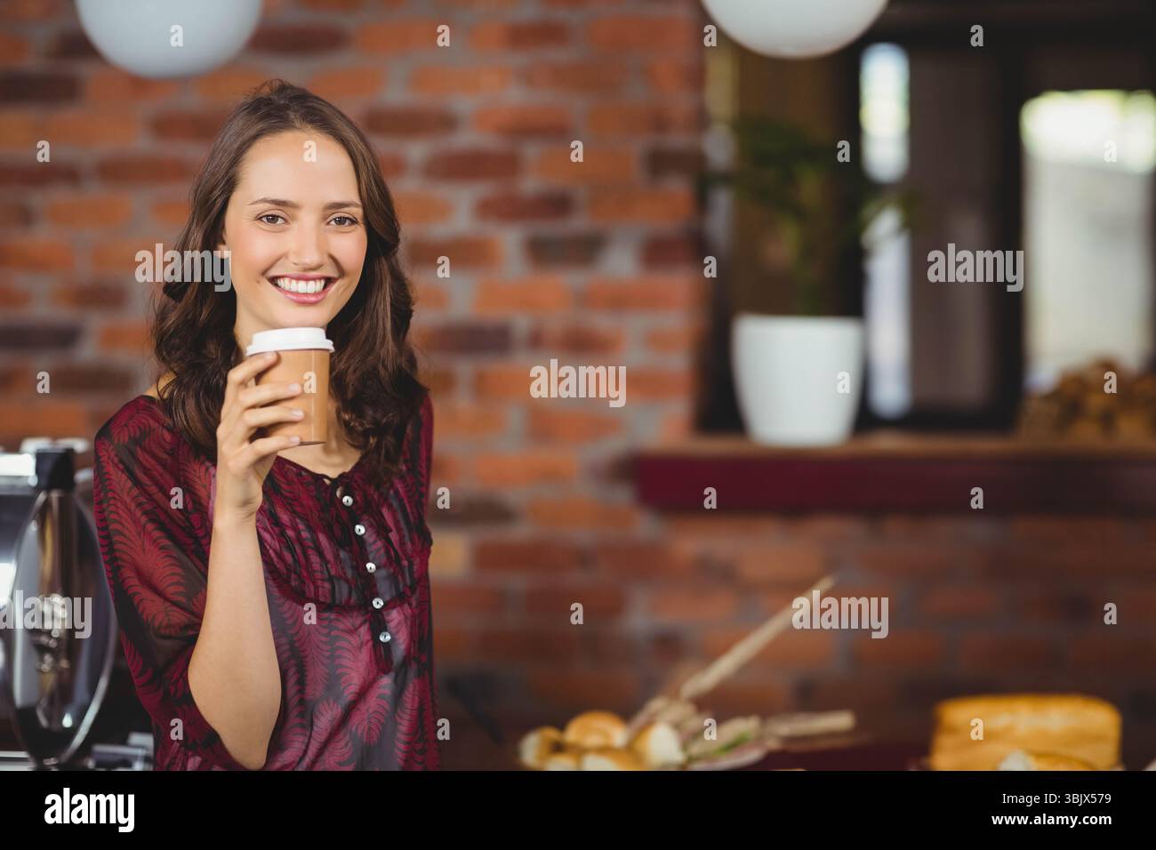 Barista tenant une tasse à café à emporter derrière le comptoir du café avec pâtisseries et machine à espresso Banque D'Images