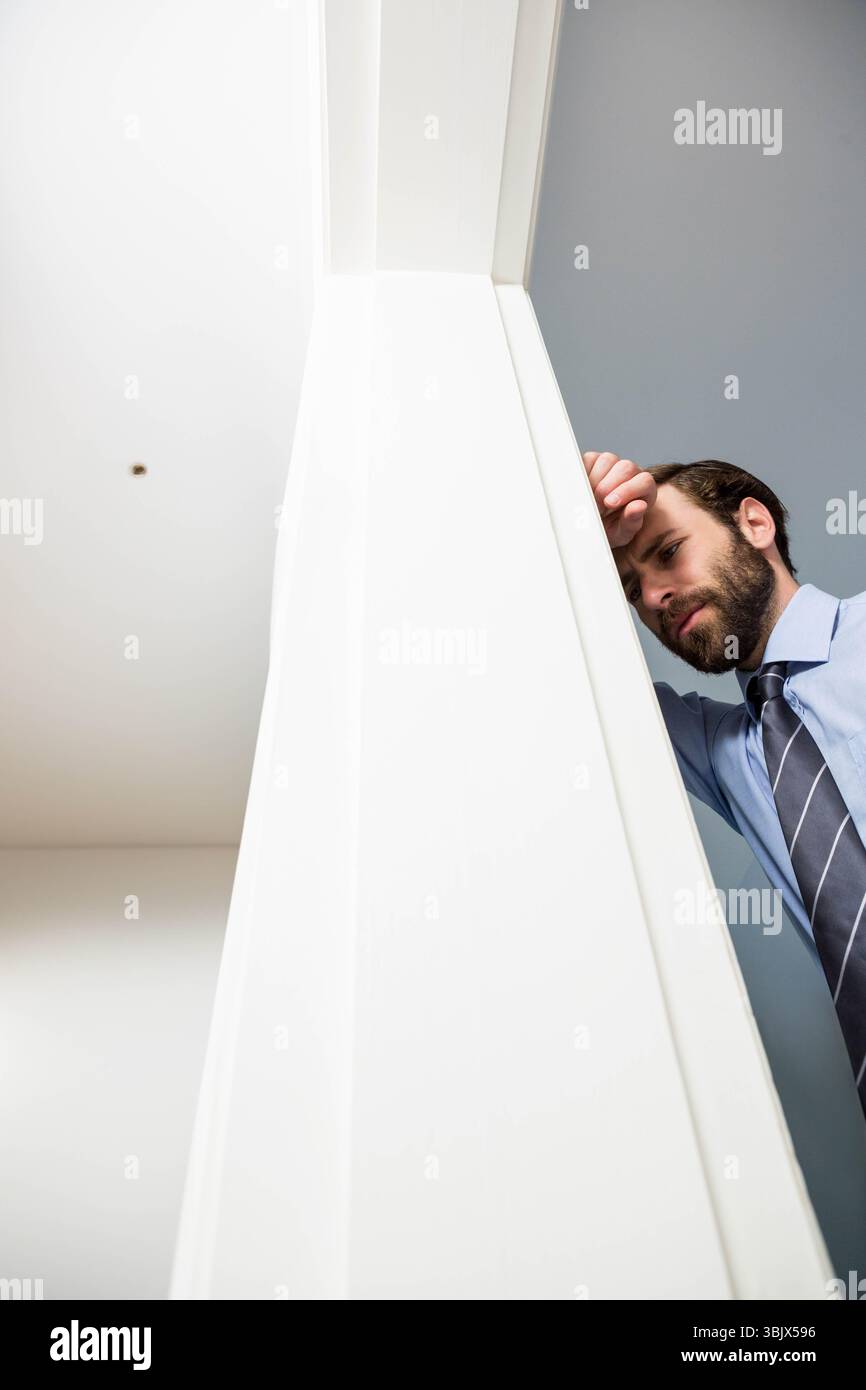 Homme en chemise appuyé contre le cadre de porte blanc dans le couloir reposant le front sur la main sous l'applique murale Banque D'Images