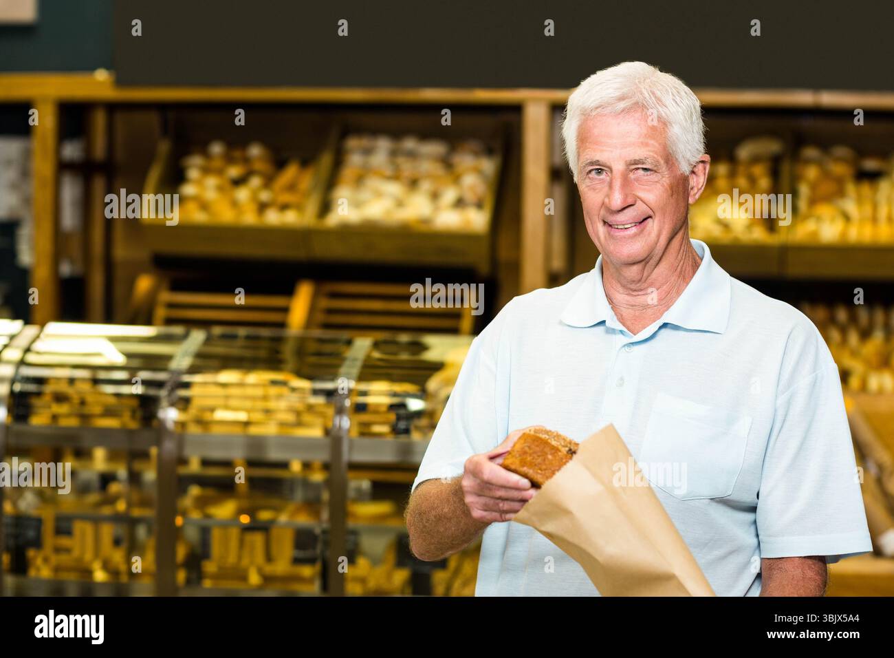 Homme senior souriant et tenant la miche de pain dans un sac en papier à l'intérieur d'une boulangerie, espace de copie Banque D'Images
