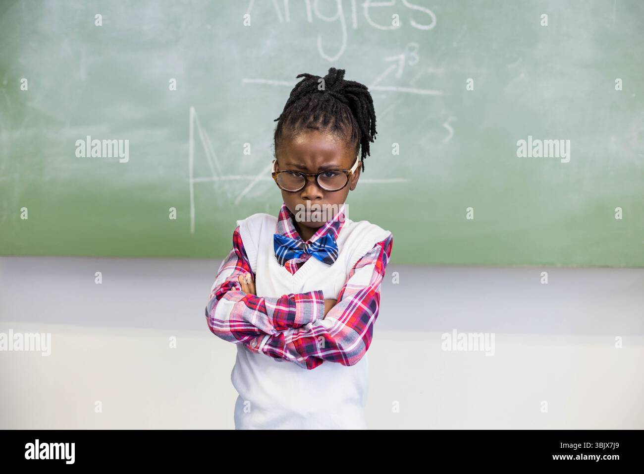 L'écolière est debout devant un tableau vert avec des diagrammes de géométrie et de la poussière de craie sur le rebord Banque D'Images