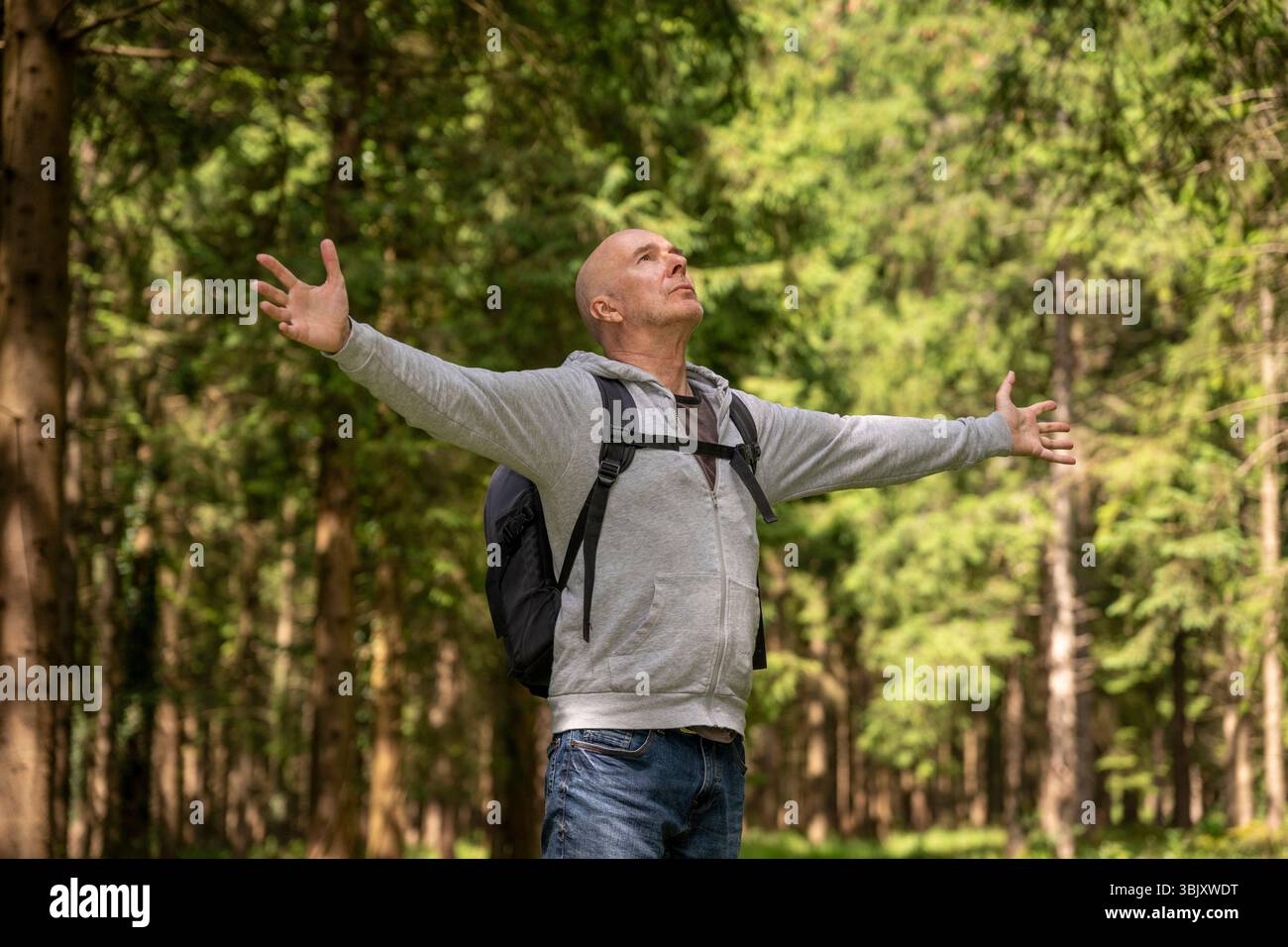 Un homme avec un sac à dos étire les bras, appréciant l'air frais et la beauté de la nature dans une forêt verdoyante. Banque D'Images