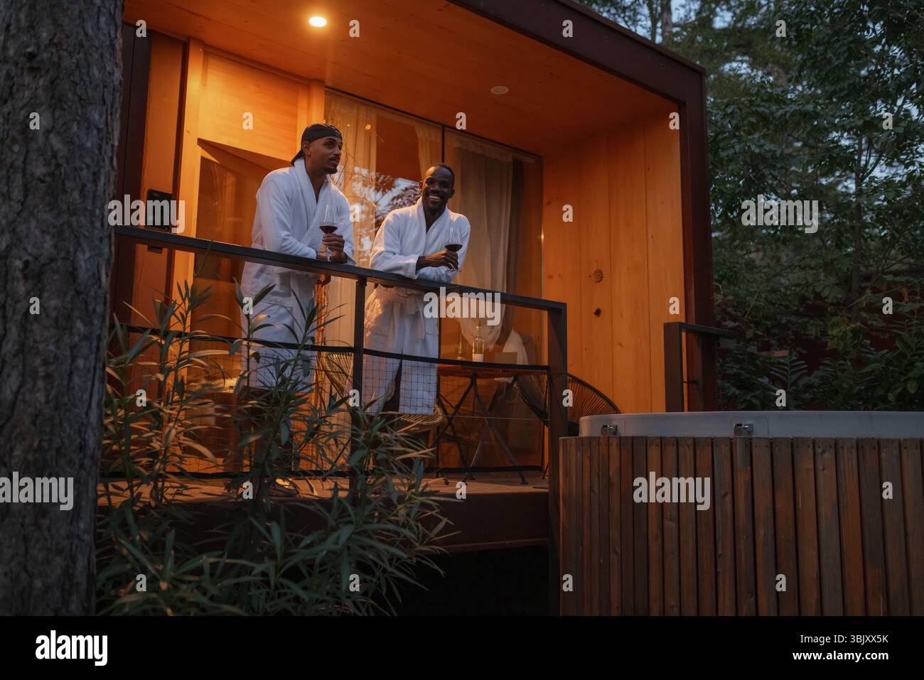 Couple gay afro-américain masculin LGBT lors d'une escapade de week-end, profitant d'un hébergement glamping, toast et clinking lunettes tout en se tenant debout sur un Banque D'Images
