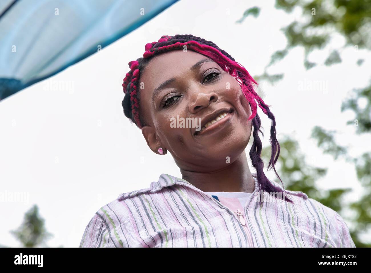 Éducateur de maternelle noir amical avec coiffure protectrice colorée en chemise rayée, parfait pour les concepts éducatifs Banque D'Images