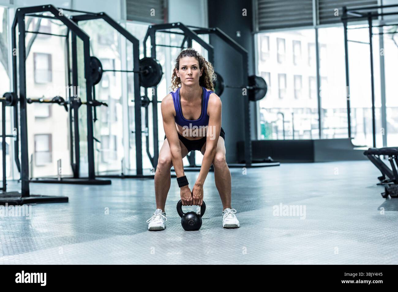 Femme effectuant un squat kettlebell dans la zone de gymnastique en vêtements de sport avec des supports de squat et des plaques de poids Banque D'Images