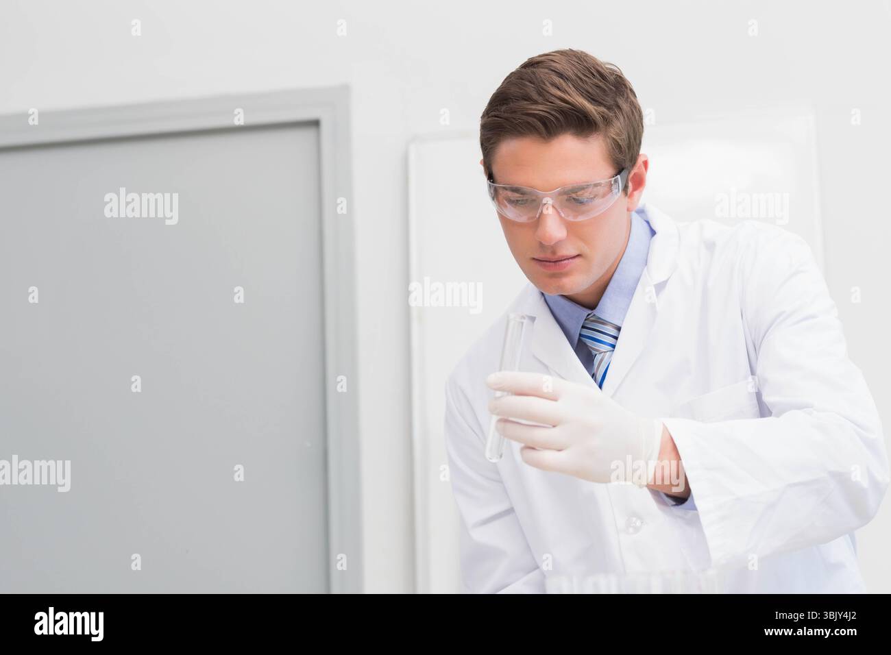 Scientifique masculin examinant un tube à essai transparent dans un laboratoire de recherche portant une blouse de laboratoire et des lunettes, copiez l'espace Banque D'Images