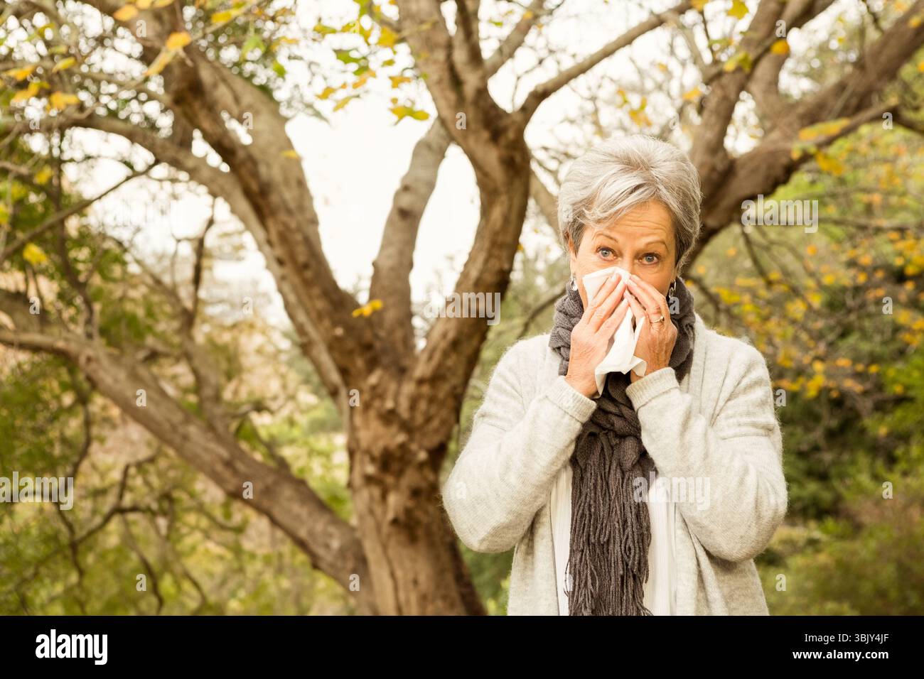 Femme âgée debout dans le parc parmi les arbres jaunes d'automne tenant le tissu au nez, copiez l'espace Banque D'Images