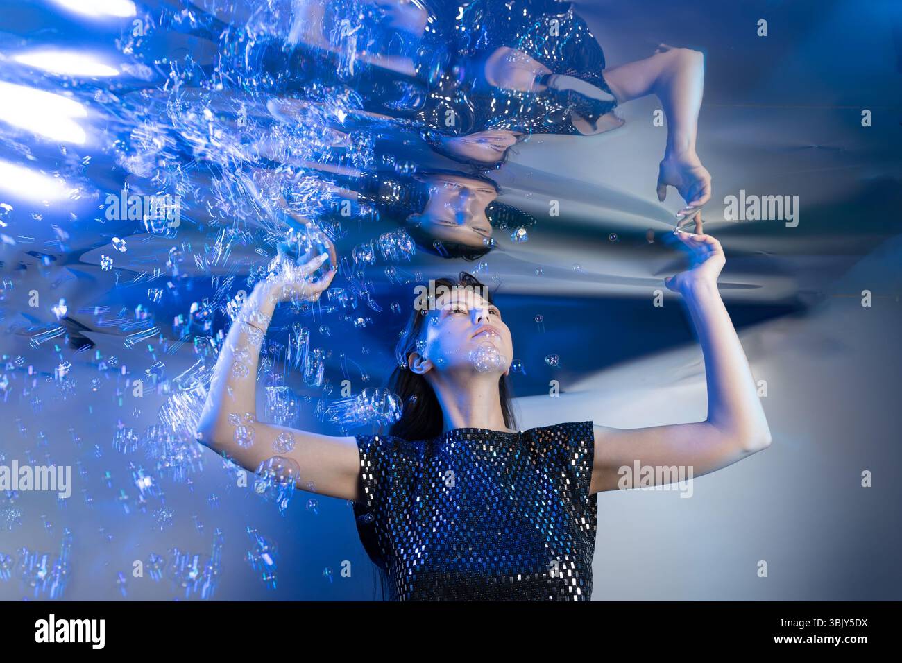 Une fille habillée comme une sirène capte l'attention tout en étant submergée dans l'eau claire. Des bulles l'entourent, ajoutant à l'ambiance fantastique du monde sous-marin qu'elle habite. Banque D'Images