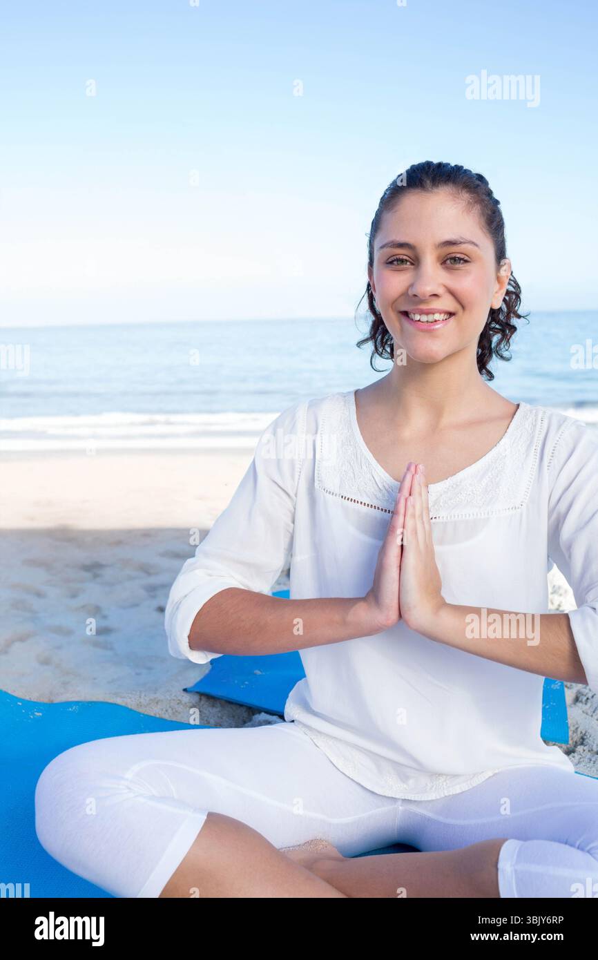 Femme méditant les jambes croisées sur le tapis de yoga bleu sur la plage de sable par les vagues calmes de l'océan, espace copie Banque D'Images