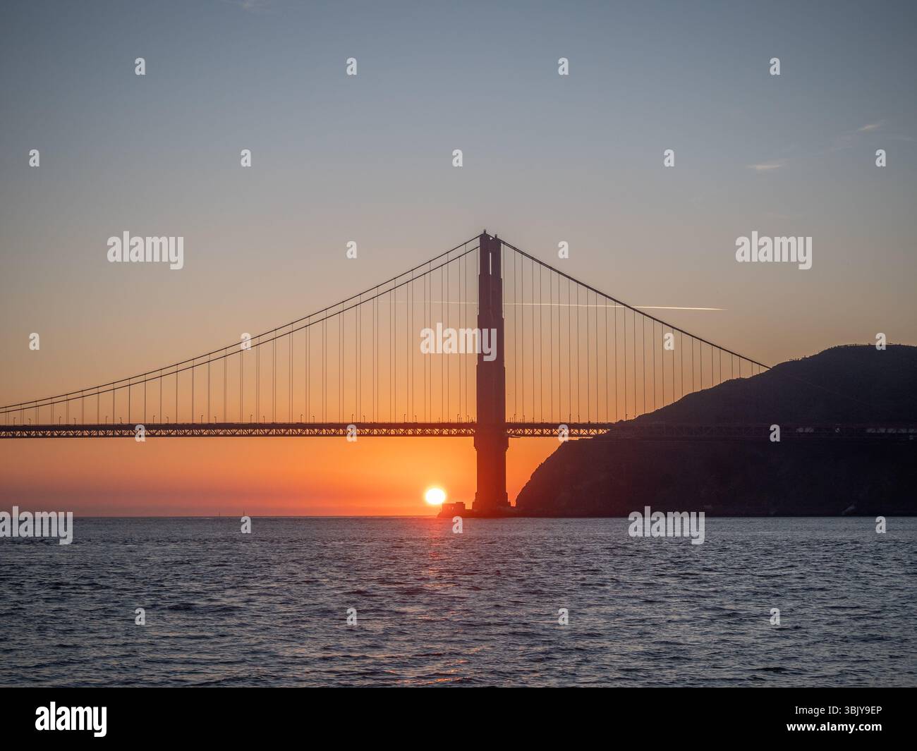 Le soleil se couche derrière le Golden Gate Bridge, projetant une lueur chaude sur l'eau et dessinant la structure emblématique du pont. Banque D'Images Le soleil se couche derrière le Golden Gate Bridge, projetant une lueur chaude sur l'eau et dessinant la structure emblématique du pont. Banque D'Images