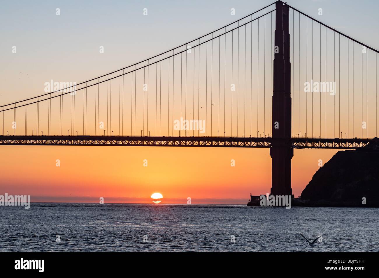 Le Golden Gate Bridge se silhouette contre un coucher de soleil vibrant, avec le soleil semblant plonger sous l'horizon, créant un contraste saisissant entre la structure sombre et les couleurs chaudes du ciel et de l'eau. Banque D'Images Le Golden Gate Bridge se silhouette contre un coucher de soleil vibrant, avec le soleil semblant plonger sous l'horizon, créant un contraste saisissant entre la structure sombre et les couleurs chaudes du ciel et de l'eau. Banque D'Images