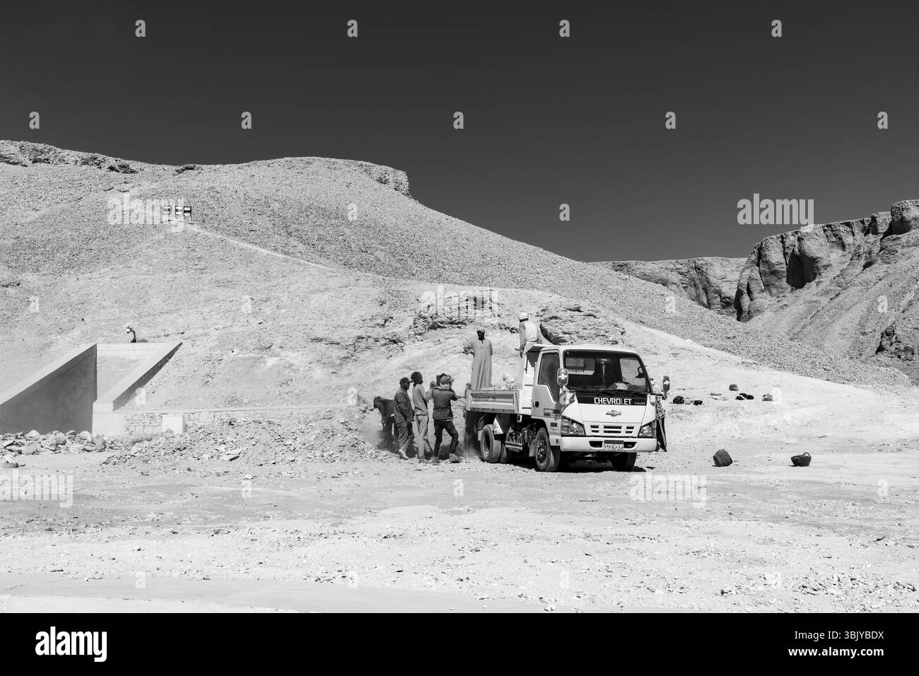 Un groupe d'hommes charge des roches à l'arrière d'un camion Chevrolet dans un paysage désertique, peut-être à des fins de construction ou d'excavation. Banque D'Images