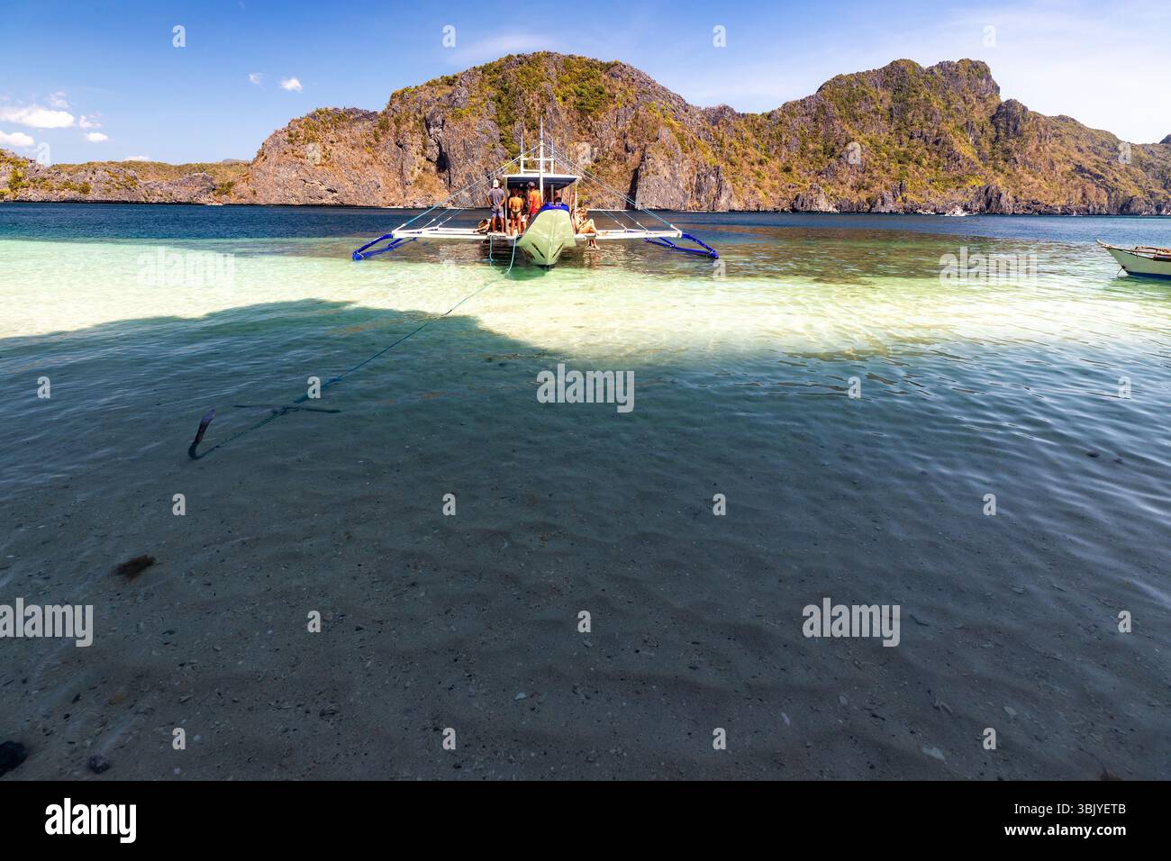 Un groupe de personnes se trouve sur un bateau en eau peu profonde près d'une île rocheuse, profitant probablement d'une journée de saut d'île ou de plongée en apnée dans un endroit tropical. Banque D'Images