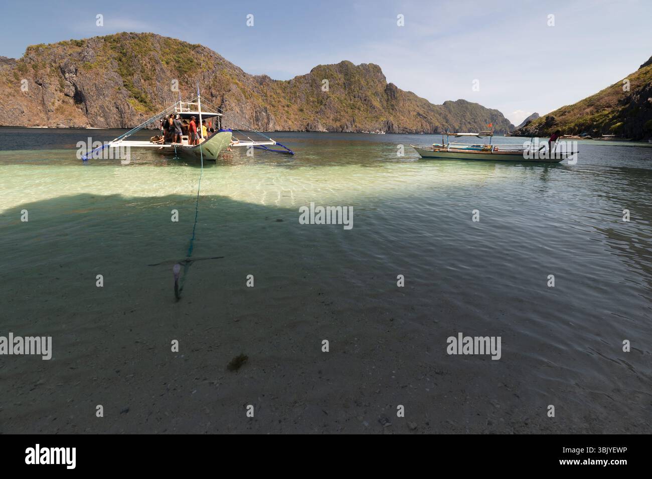 Un groupe de personnes est sur un bateau ancré dans une eau peu profonde près d'une île rocheuse. Un autre bateau est à proximité, et l'eau est claire et bleue. Banque D'Images