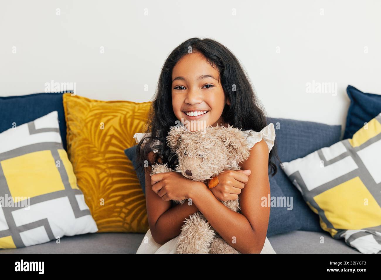 Fille souriante tient un jouet et regarde la caméra. Petite fille embrassant un ours en peluche tout en étant assise sur le canapé. Banque D'Images Fille souriante tient un jouet et regarde la caméra. Petite fille embrassant un ours en peluche tout en étant assise sur le canapé. Banque D'Images