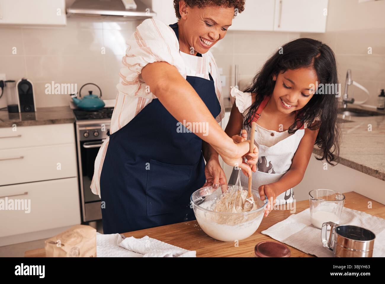 Bonne grand-mère enseignant à la petite-fille comment préparer la pâte pour les petits gâteaux Banque D'Images Bonne grand-mère enseignant à la petite-fille comment préparer la pâte pour les petits gâteaux Banque D'Images