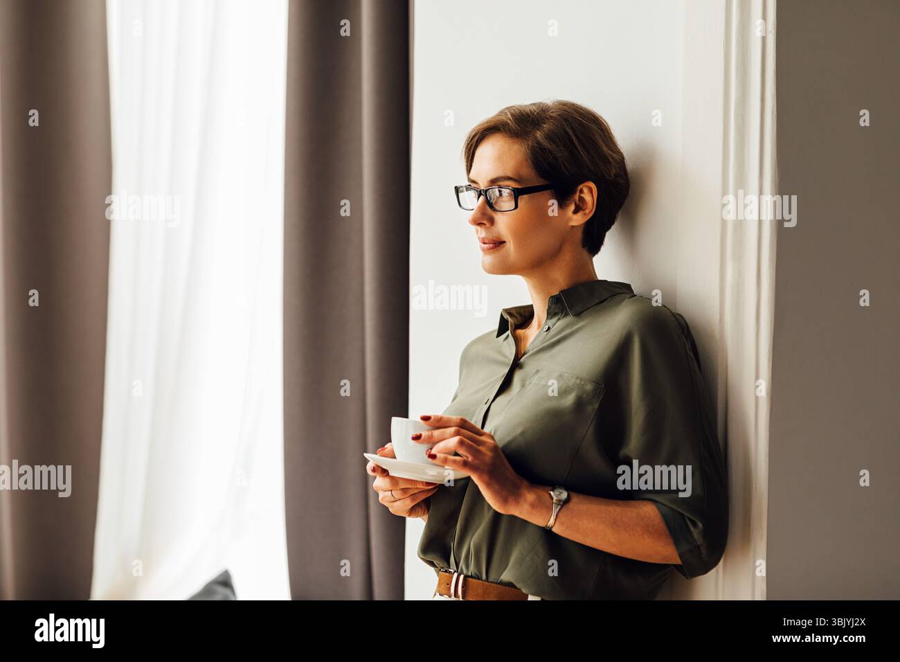 Femme de race blanche d'âge adulte dans des vêtements habillés debout dans l'appartement chambre et avoir une tasse de café Banque D'Images Femme de race blanche d'âge adulte dans des vêtements habillés debout dans l'appartement chambre et avoir une tasse de café Banque D'Images