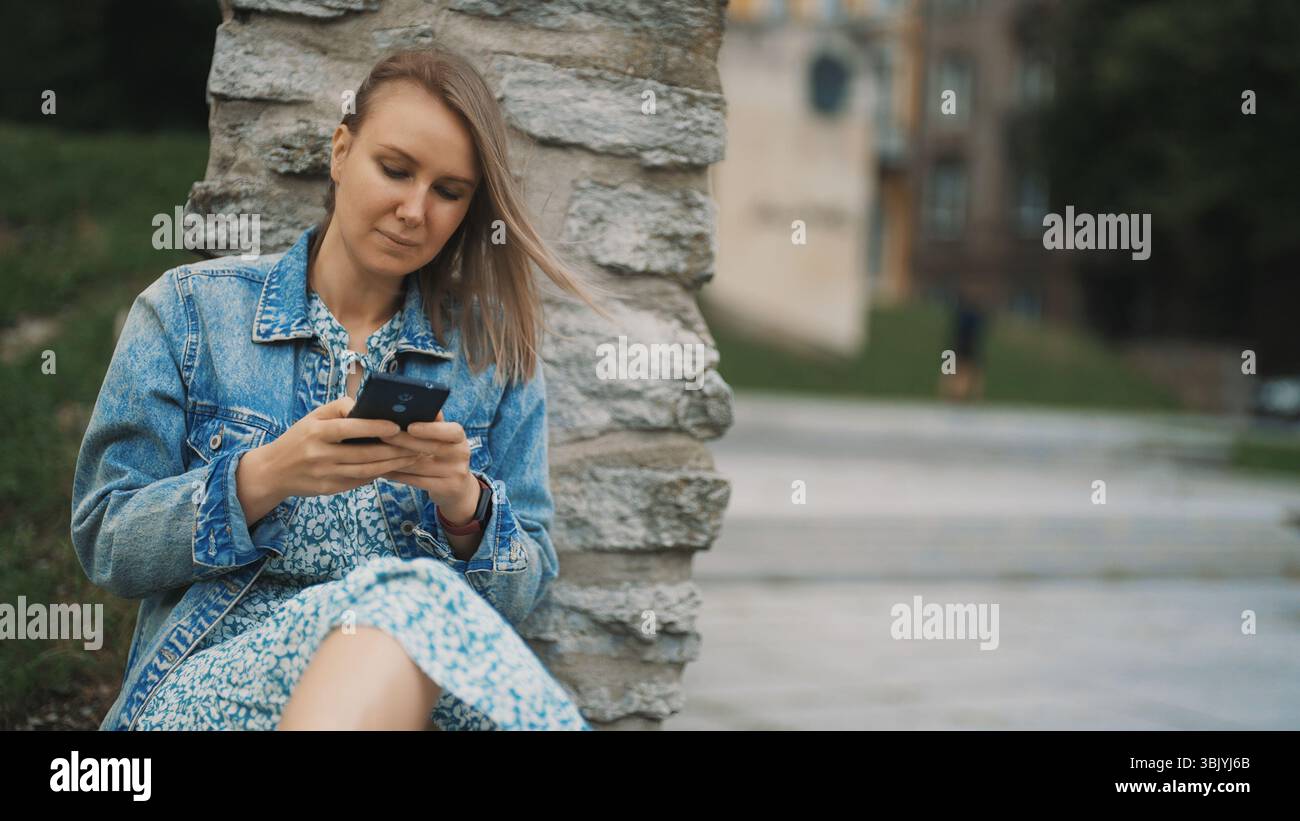 Une femme avec un smartphone se repose dans la vieille ville. Banque D'Images Une femme avec un smartphone se repose dans la vieille ville. Banque D'Images