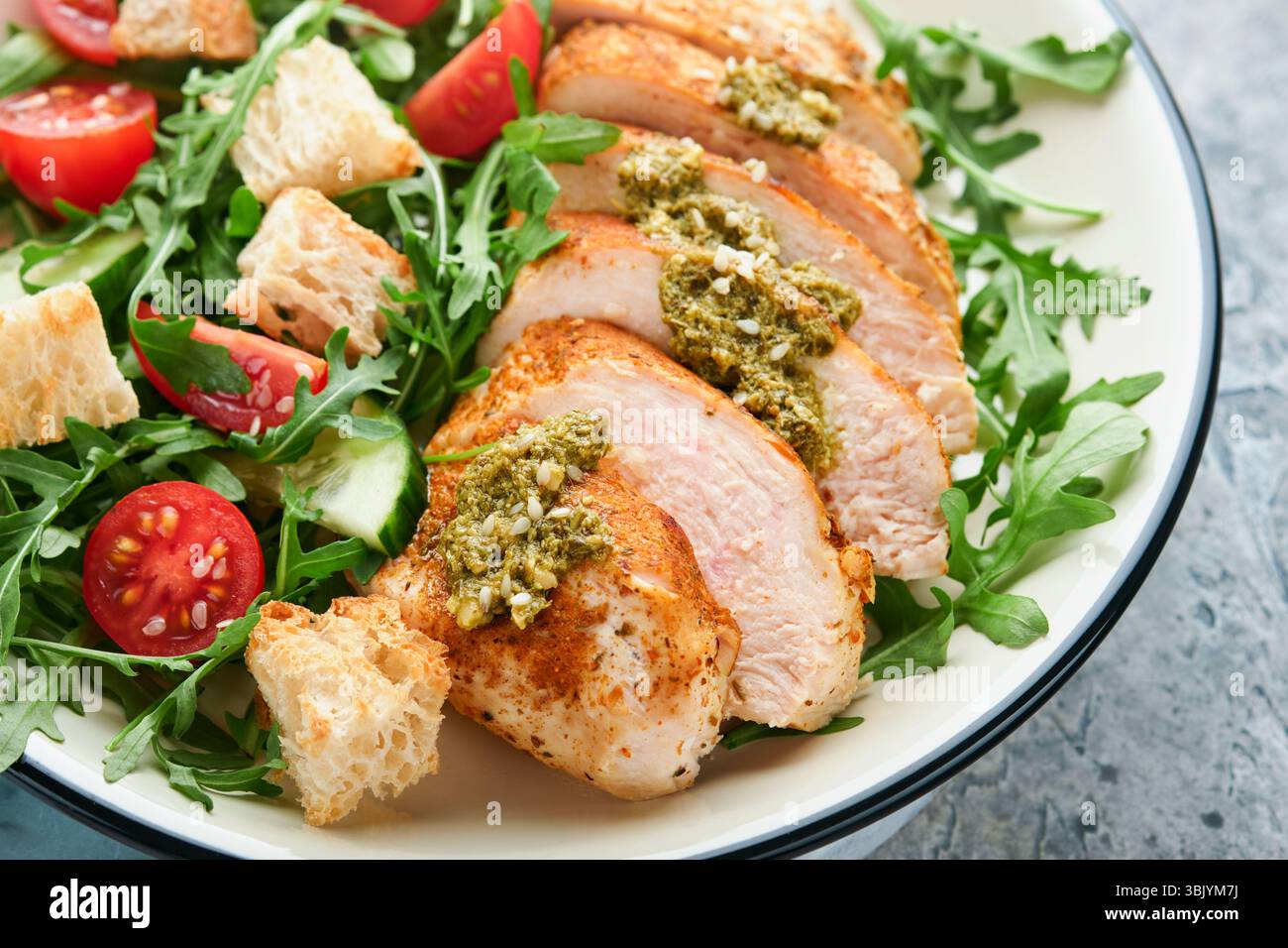 Salade fraîche avec filet de poulet grillé, roquette, tomates, concombre et sauce pesto, graines de sésame avec huile d'olive dans un bol blanc Banque D'Images Salade fraîche avec filet de poulet grillé, roquette, tomates, concombre et sauce pesto, graines de sésame avec huile d'olive dans un bol blanc Banque D'Images