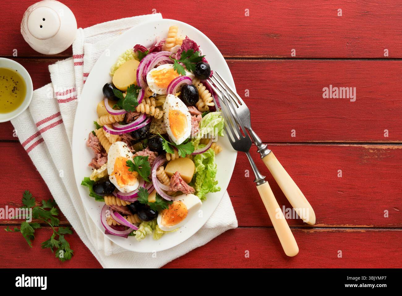 Salade de thon avec pâtes, œufs, pommes de terre, olives, oignons rouges et sauce dans une assiette blanche sur fond de table rustique rouge vieux. Nicoise s Banque D'Images Salade de thon avec pâtes, œufs, pommes de terre, olives, oignons rouges et sauce dans une assiette blanche sur fond de table rustique rouge vieux. Nicoise s Banque D'Images
