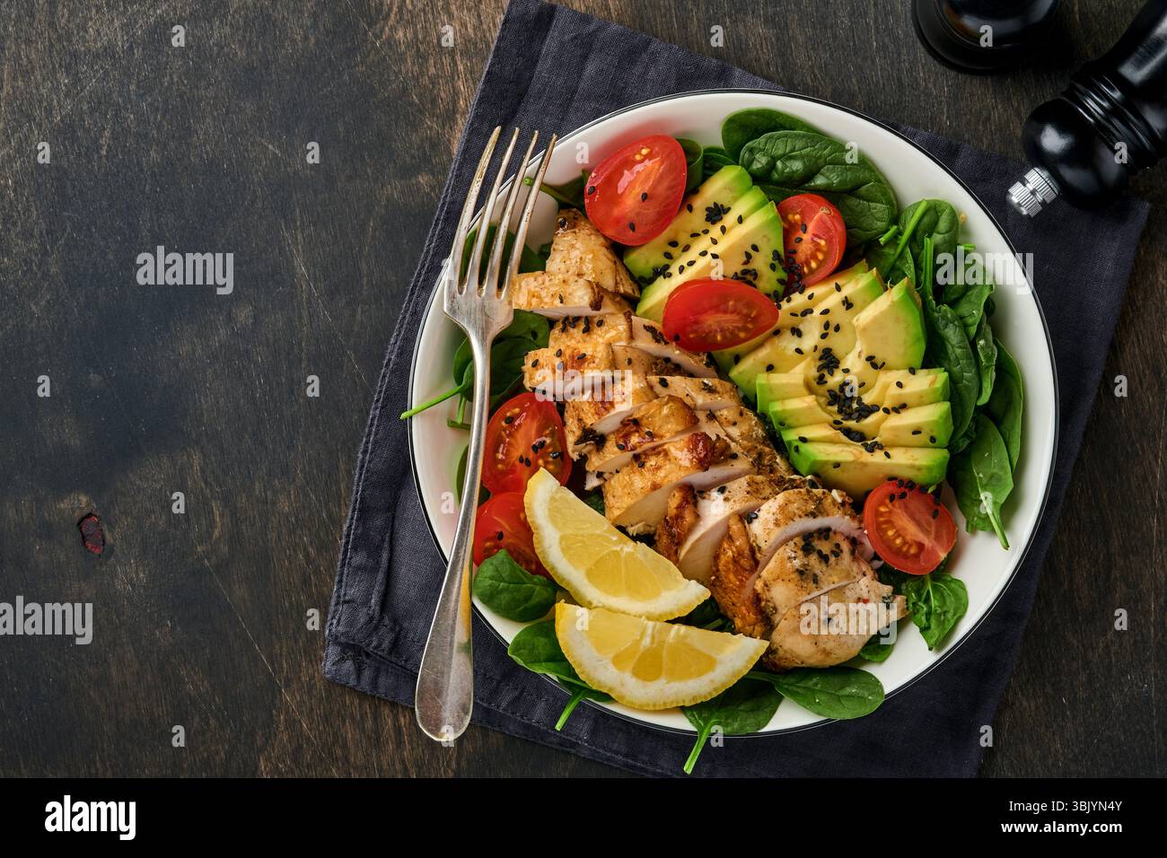 Salade verte fraîche avec filet de poulet grillé, épinards, tomates, avocat, citron et graines de sésame noir dans un bol blanc sur vieux woo Banque D'Images Salade verte fraîche avec filet de poulet grillé, épinards, tomates, avocat, citron et graines de sésame noir dans un bol blanc sur vieux woo Banque D'Images