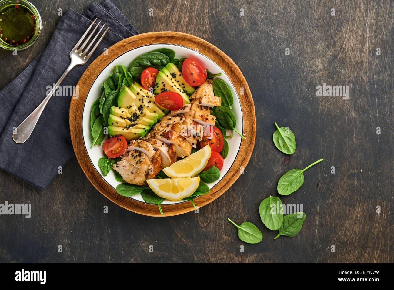 Salade verte fraîche avec filet de poulet grillé, épinards, tomates, avocat, citron et graines de sésame noir dans un bol blanc sur vieux woo Banque D'Images Salade verte fraîche avec filet de poulet grillé, épinards, tomates, avocat, citron et graines de sésame noir dans un bol blanc sur vieux woo Banque D'Images