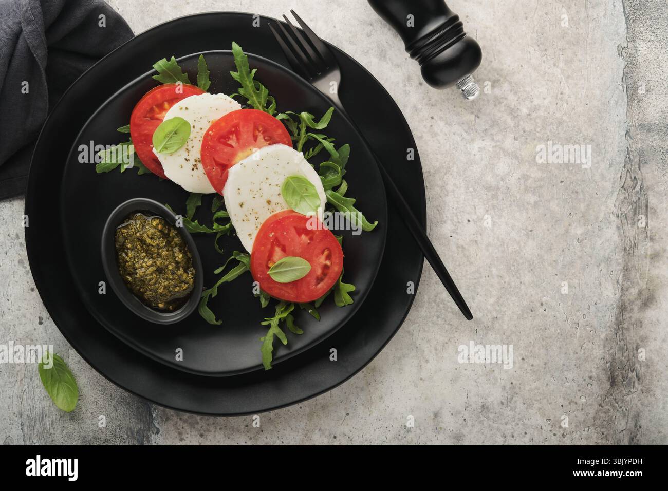 Salade Caprese. Salade italienne caprese avec tomates tranchées, fromage mozzarella, roquette, basilic, huile d'olive dans une assiette noire sur vieux Banque D'Images Salade Caprese. Salade italienne caprese avec tomates tranchées, fromage mozzarella, roquette, basilic, huile d'olive dans une assiette noire sur vieux Banque D'Images
