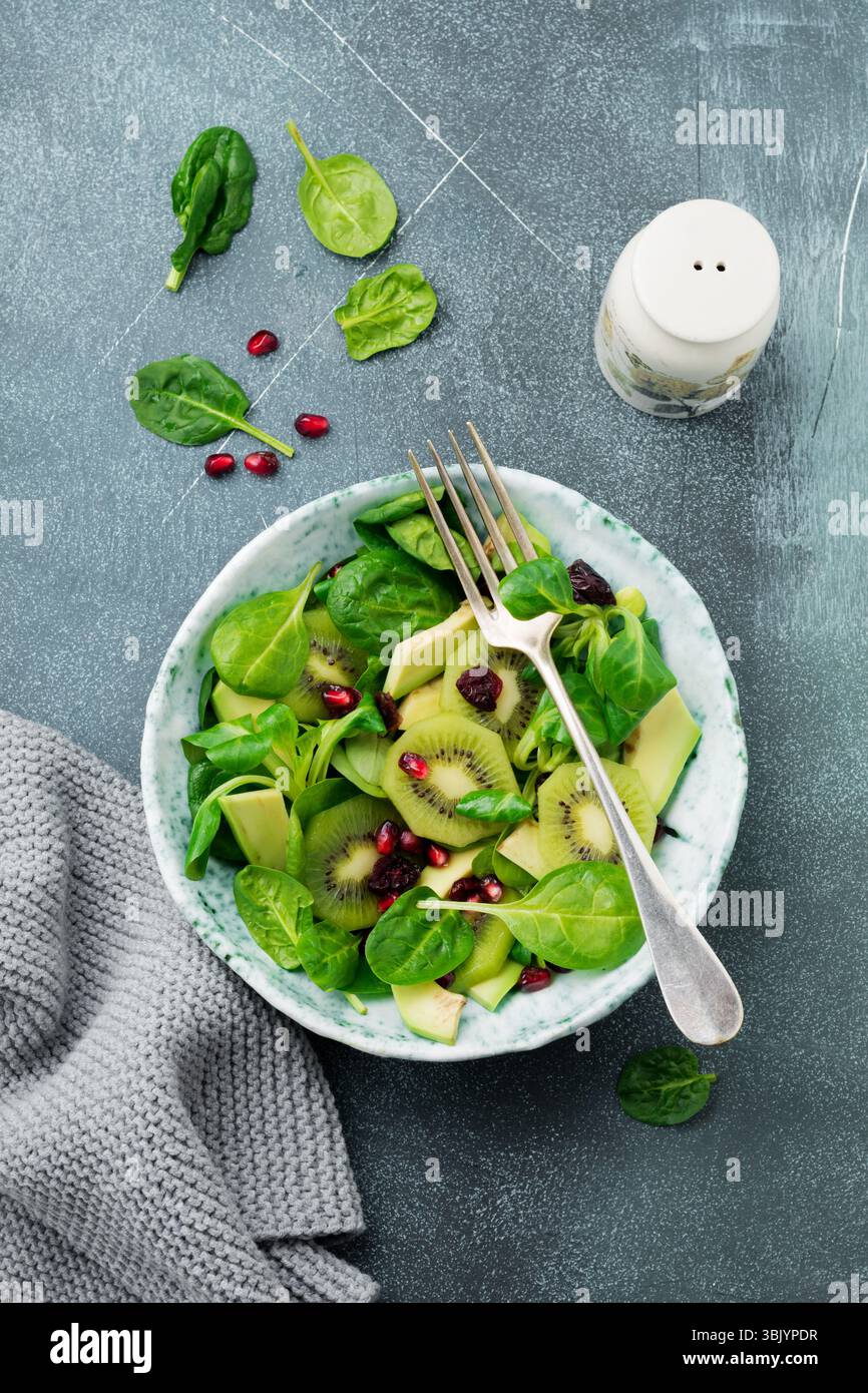 Salade de feuilles de bébé d'épinards, cresson, kiwi, avocat et grenade dans une vieille assiette en céramique sur fond de béton gris. S Banque D'Images Salade de feuilles de bébé d'épinards, cresson, kiwi, avocat et grenade dans une vieille assiette en céramique sur fond de béton gris. S Banque D'Images