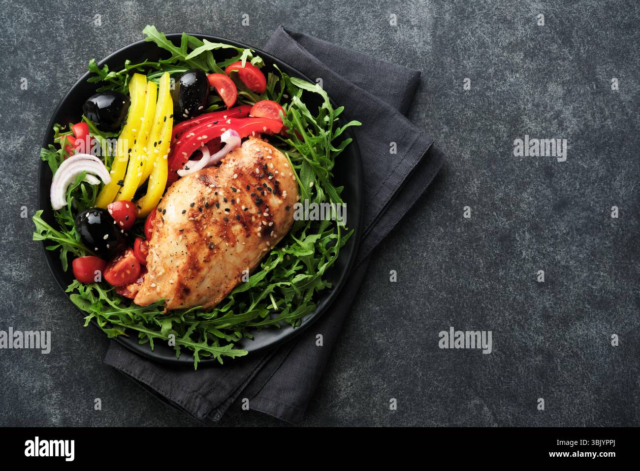 Salade avec filet de poulet grillé avec roquette fraîche, tomates et olives sur assiette noire sur fond sombre ancien. Poulet m Banque D'Images Salade avec filet de poulet grillé avec roquette fraîche, tomates et olives sur assiette noire sur fond sombre ancien. Poulet m Banque D'Images