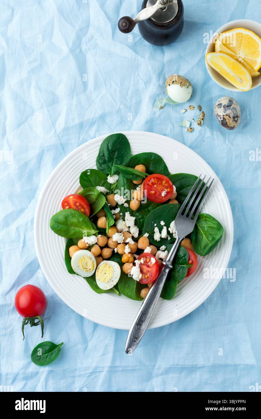 Salade végétarienne avec épinards, pois chiches, tomates cerises, oeuf et fromage feta et citron sur fond clair. Mise au point sélective. Banque D'Images Salade végétarienne avec épinards, pois chiches, tomates cerises, oeuf et fromage feta et citron sur fond clair. Mise au point sélective. Banque D'Images