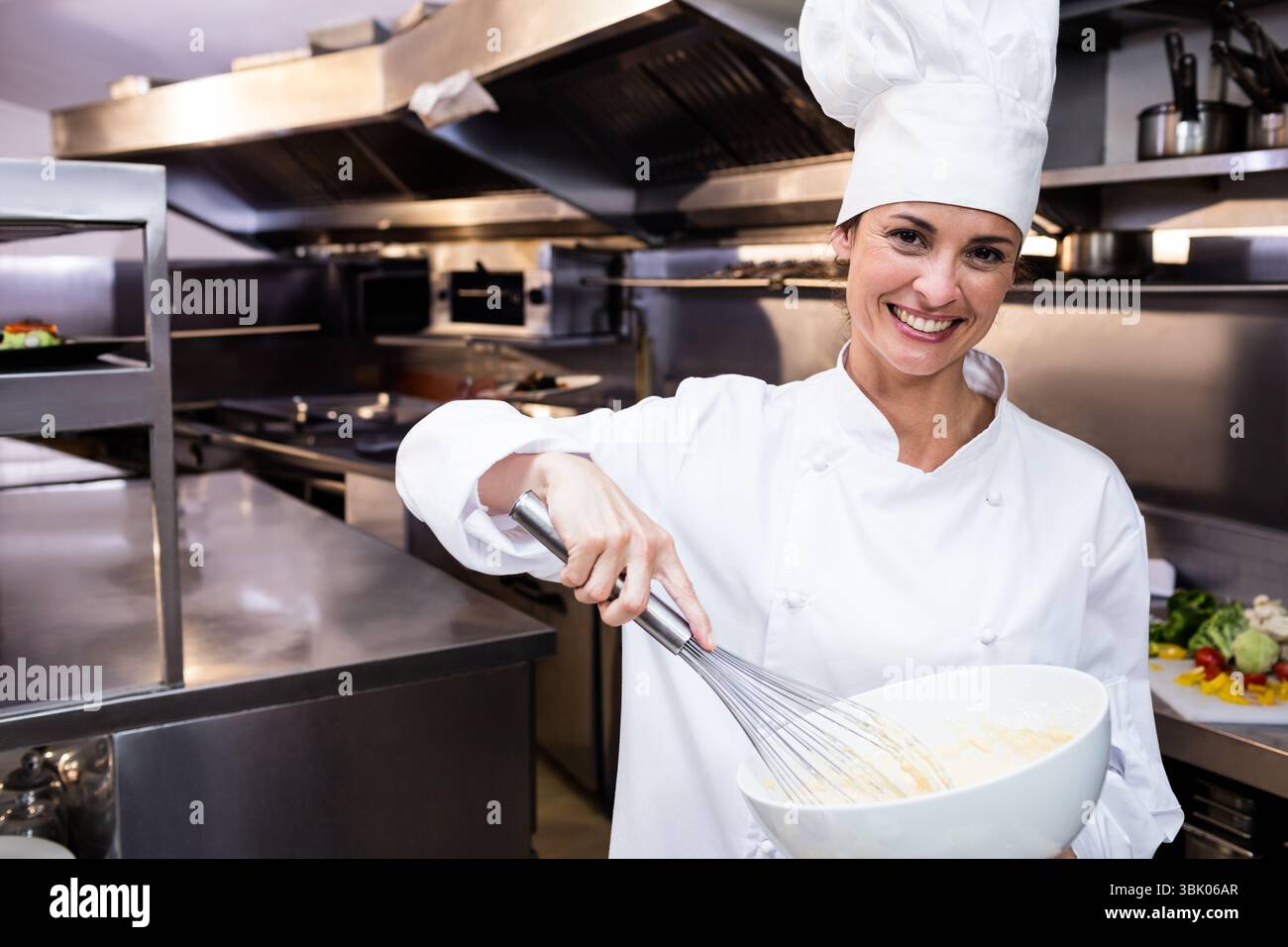 Fouet métallique fouettant la pâte crémeuse dans un grand bol blanc sur le poste de travail en acier dans la cuisine commerciale Banque D'Images