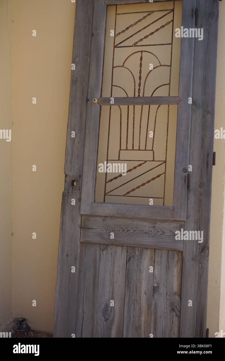 Une vieille porte décorative en bois, appuyée contre un mur jaune pâle. La porte dispose d'un panneau de verre avec un design géométrique et linéaire complexe Banque D'Images