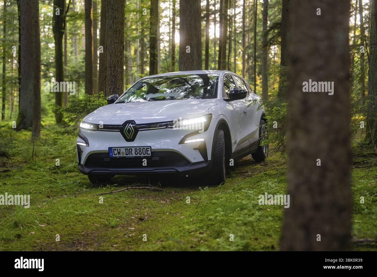 Voiture blanche dans la lumière pénétrante du soleil dans une forêt verdoyante, Renault Megane, Deer E Carsharing, voiture électrique, Calw, forêt Noire, Allemagne, Europe Banque D'Images