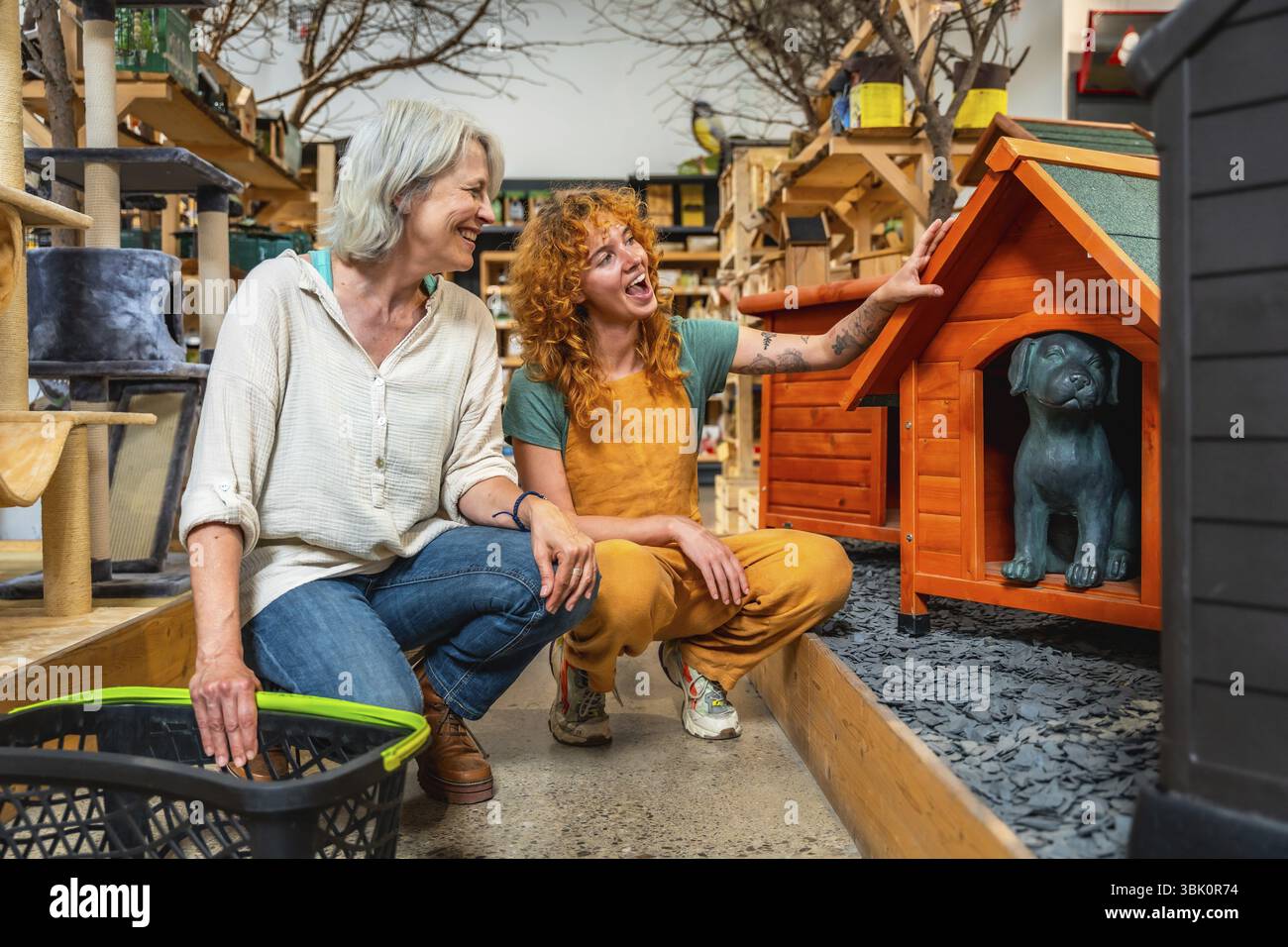 Vendeuse souriante montrant une maison de chien en bois avec une statue de chien à l'intérieur à un client tenant un panier dans une animalerie Banque D'Images
