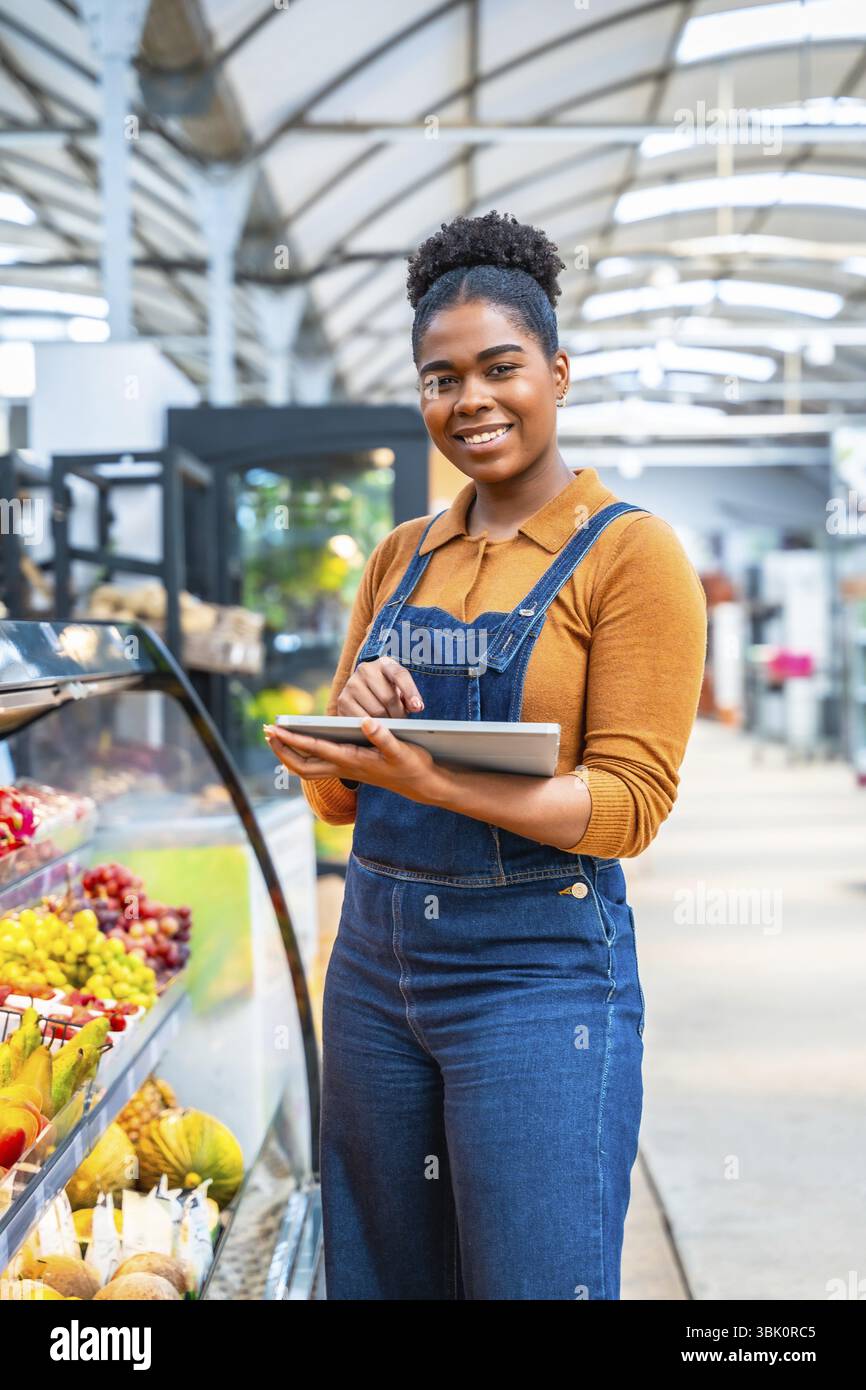 Jeune employé de supermarché gérant l'inventaire de la section des fruits frais à l'aide d'une tablette numérique, assurant la qualité et la disponibilité pour les clients Banque D'Images