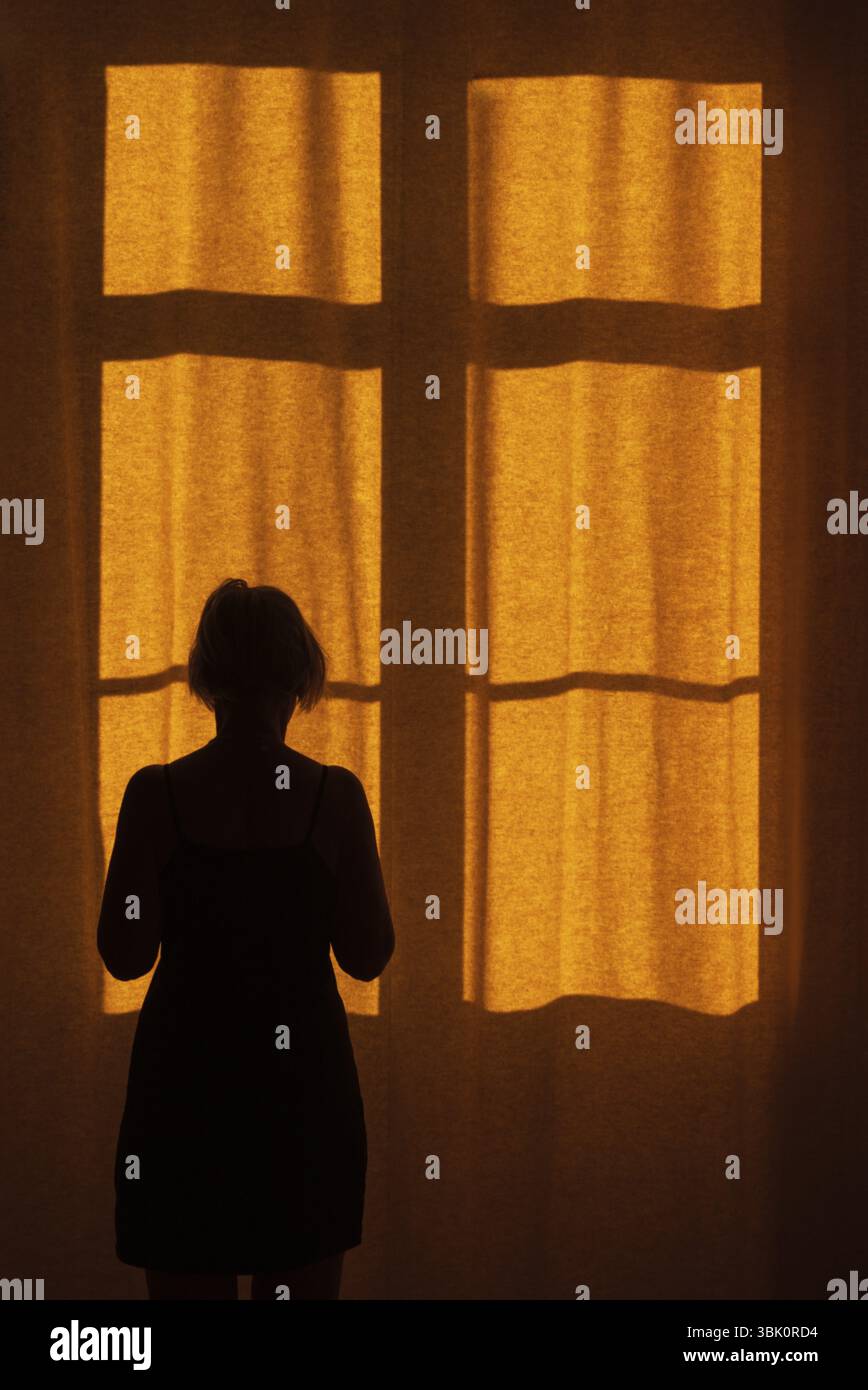 Vue arrière d'une femme debout devant une fenêtre avec un rideau rouge Banque D'Images