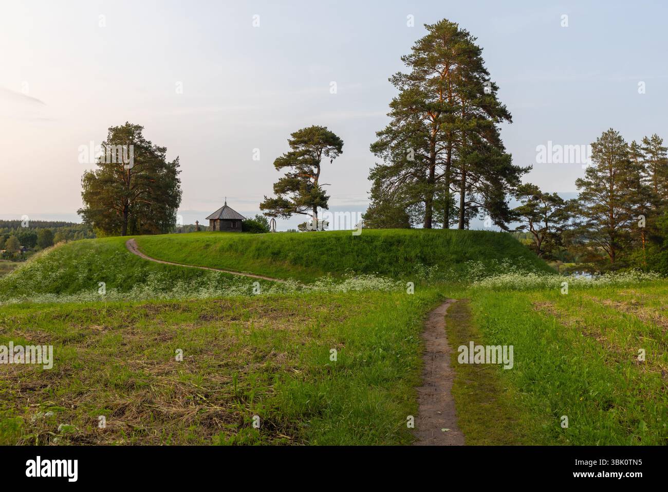 Paysage rural d'été avec une ancienne chapelle orthodoxe. Savkina gorka, région de Pskov, Russie. Un cadre de campagne pittoresque avec colline herbeuse, Banque D'Images