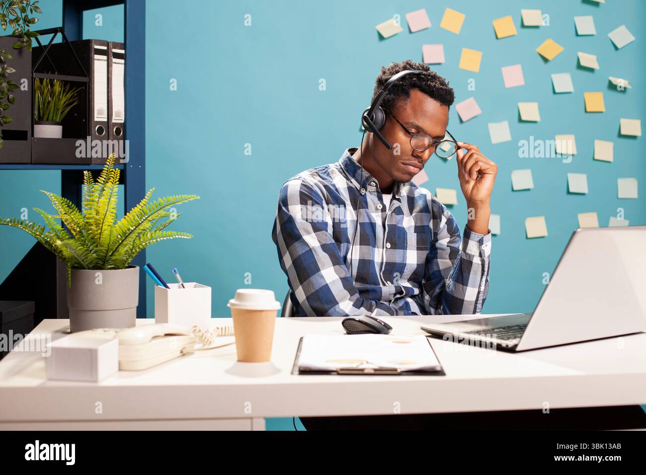 Consultant en affaires fatigué à son bureau avec son ordinateur portable, portant un casque et tenant ses lunettes. Employé épuisé profondément dans la pensée, travaillant sur un défi de projet de démarrage, essayant de trouver des solutions. Banque D'Images