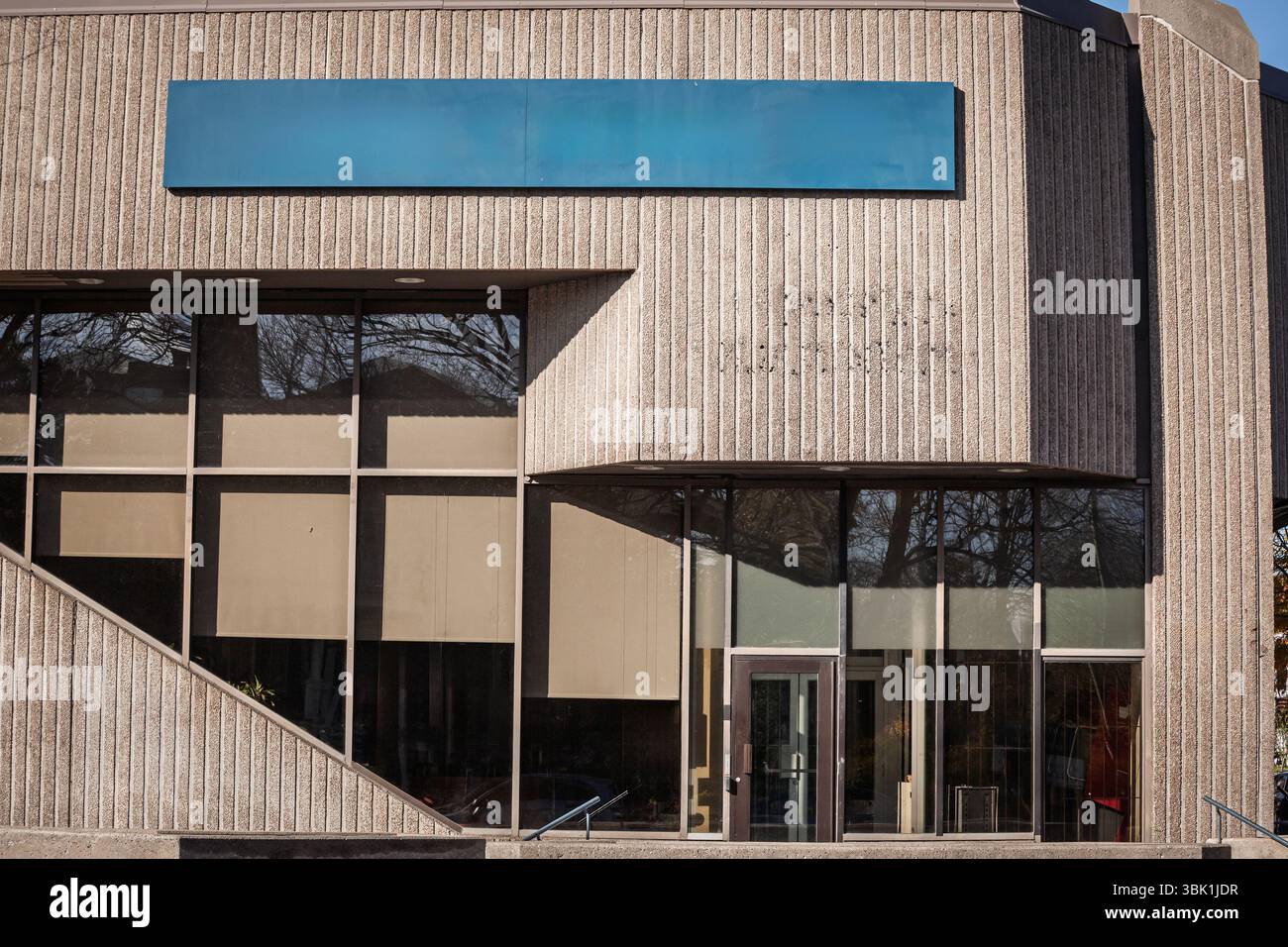Bloc de bureau en béton nervuré avec un panneau bleu vierge se tient vide par un matin ensoleillé d'hiver en Amérique du Nord, son brutaliste brutal faca du milieu du siècle Banque D'Images