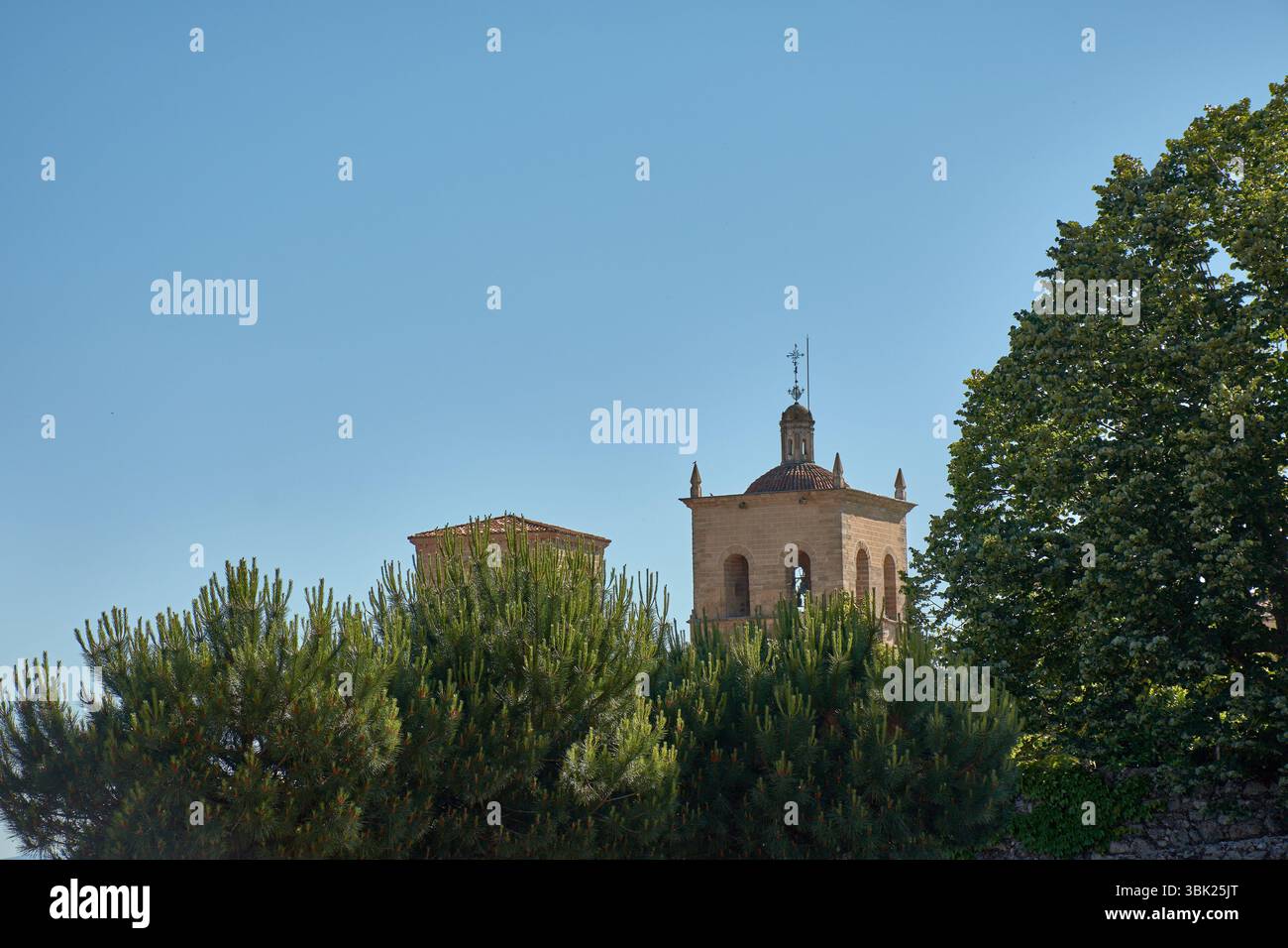 L'imposant clocher de l'église de Santa Maria la Mayor à Trujillo s'élève dans le ciel bleu, partiellement caché mais majestueux parmi le vert dense Banque D'Images