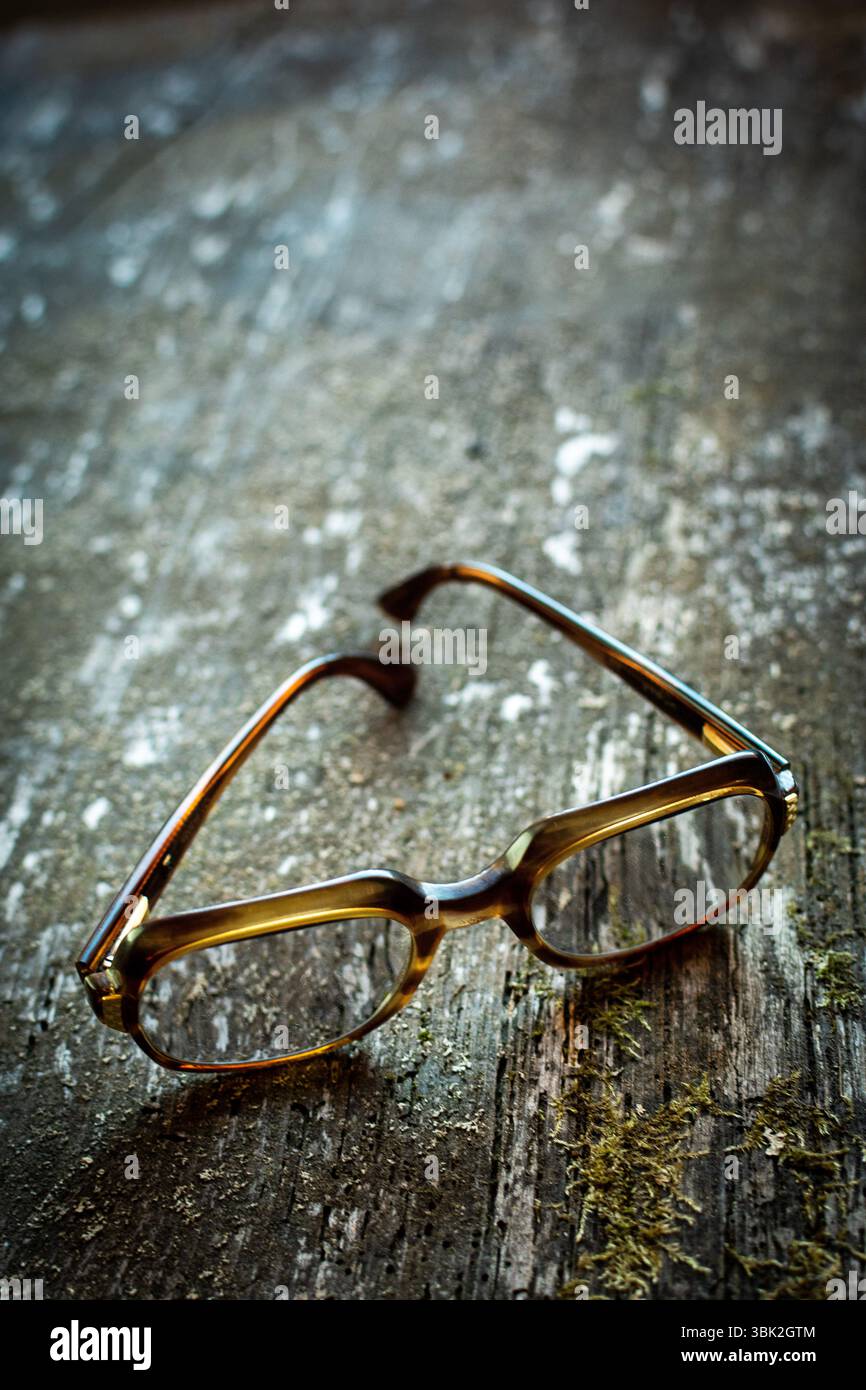 Une paire de lunettes vintage repose sur une table en bois altérée. Le design unique est éclairé par une lumière naturelle chaude, améliorant l'ambiance sereine de t Banque D'Images